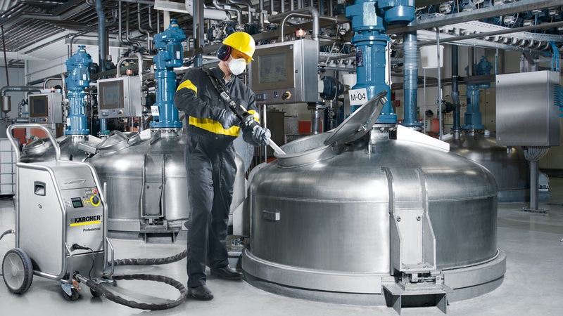 A man is working in a factory using large metal tanks for dry ice cleaning.
