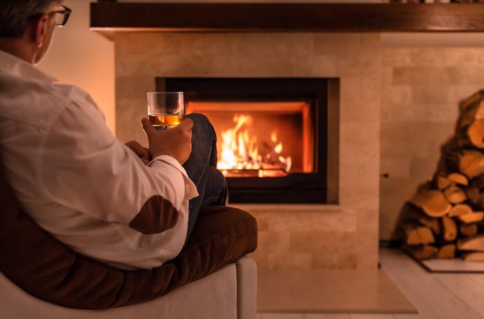 A man enjoying a glass of whiskey in front of a beautifully designed fireplace.