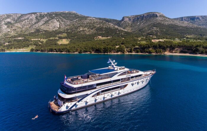 A large yacht floats near a mountain, creating a romantic destination in the blue water.