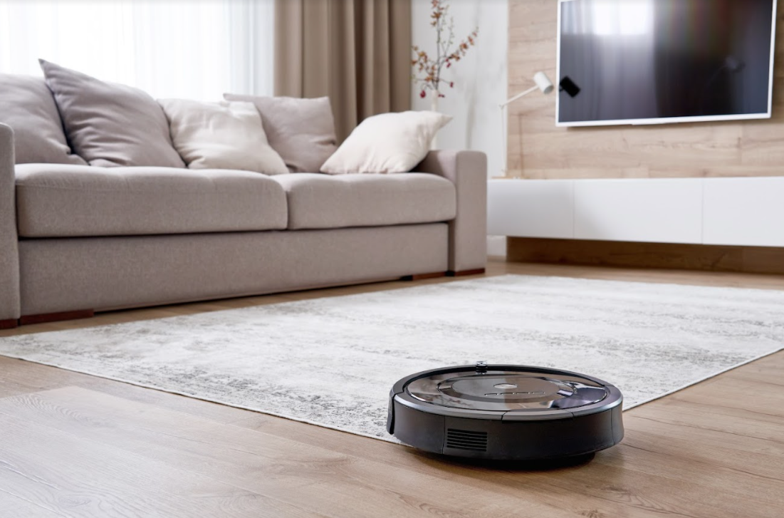 A robotic vacuum cleaner on engineered hardwood flooring in a living room.