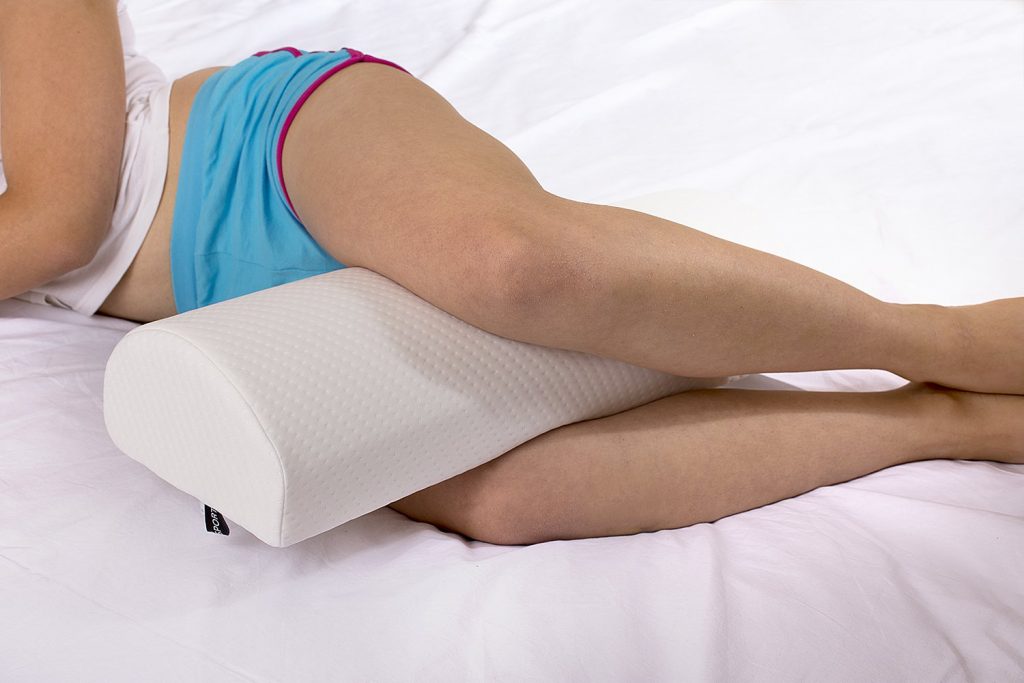 A woman using a knee pillow while sleeping on a bed.