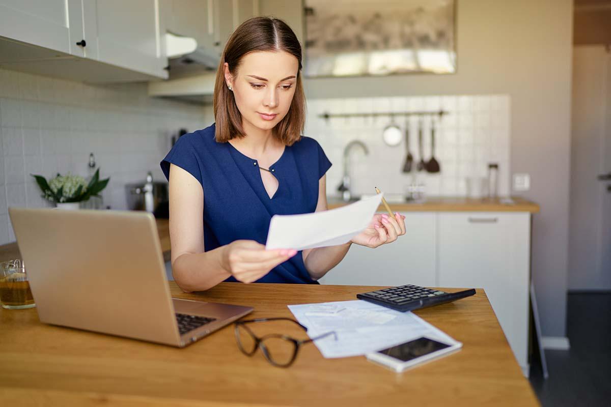 A woman sitting at a kitchen table with papers, finding ways to lower her utility bill.