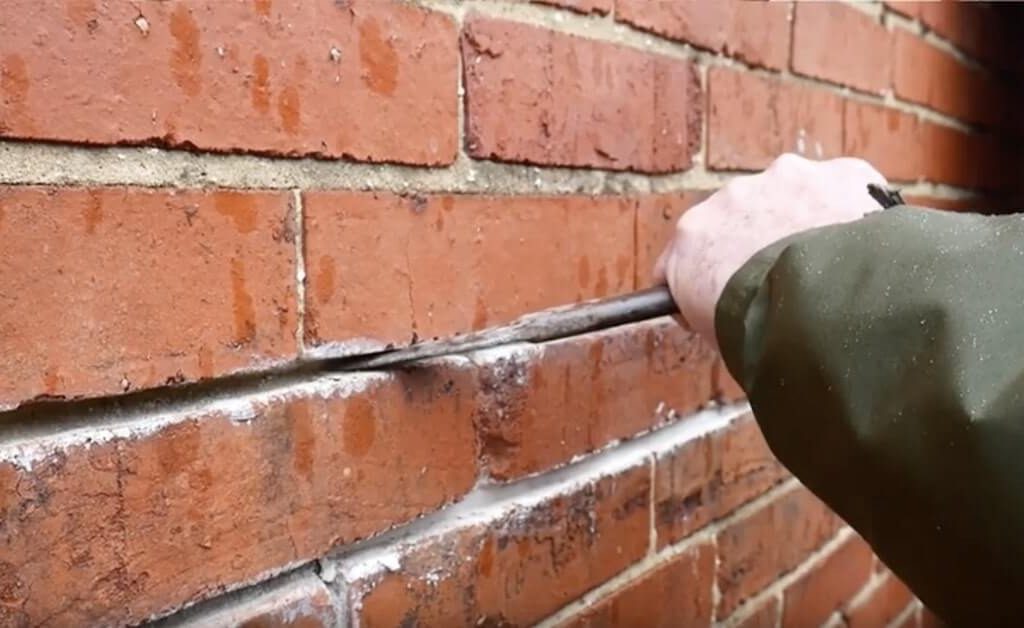 A person repairing a brick wall using a tool.