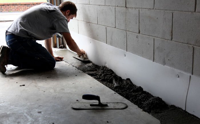 A man is working on a concrete floor in a wet garage.