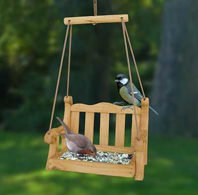 A wooden bird feeder with two birds on it in a garden during the fall.