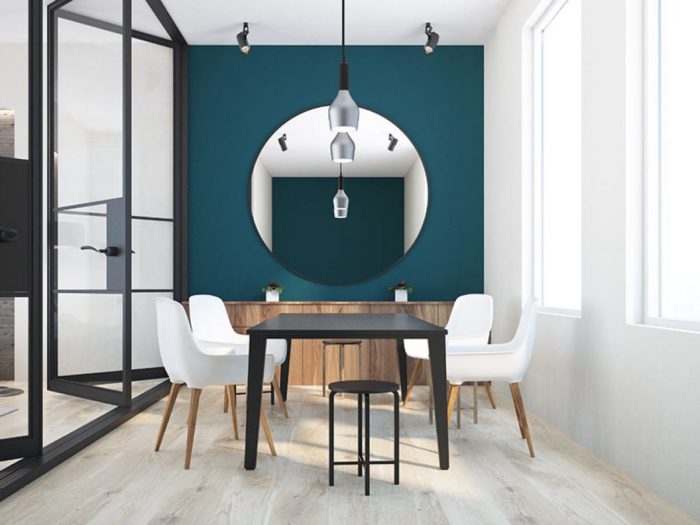 A dining room with teal walls and black furniture featuring a mirror.