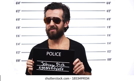 A bearded man holding up a mugshot sign.