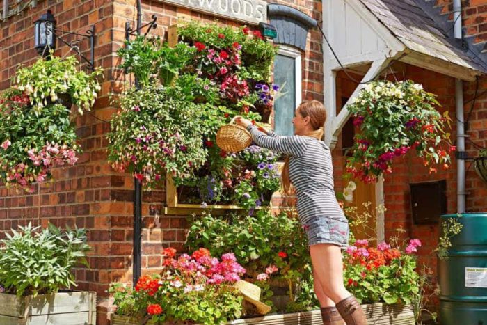 A woman is creating a garden that feels like an art installation by putting flowers in a hanging basket outside a house.