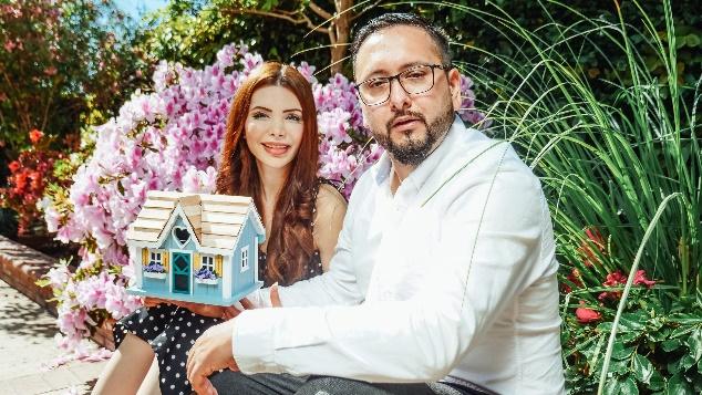 A couple holding a model house in the garden.