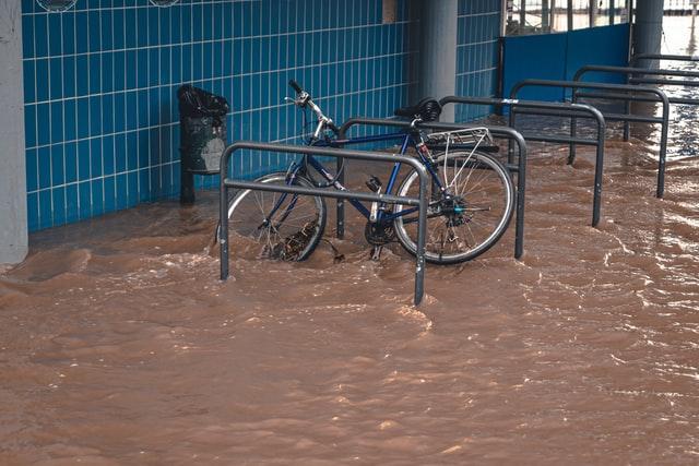 A bicycle is parked in a flooded parking lot, illustrating water damage.