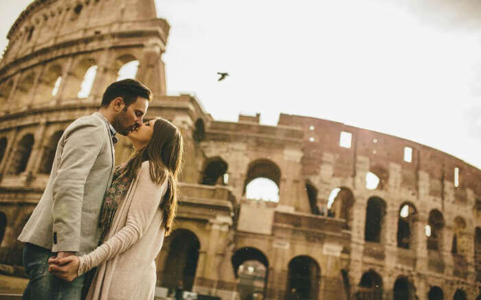 A couple kissing in front of the colossion in Rome.