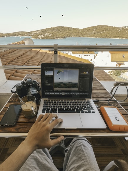 A person working remotely on a laptop on a balcony overlooking the ocean.