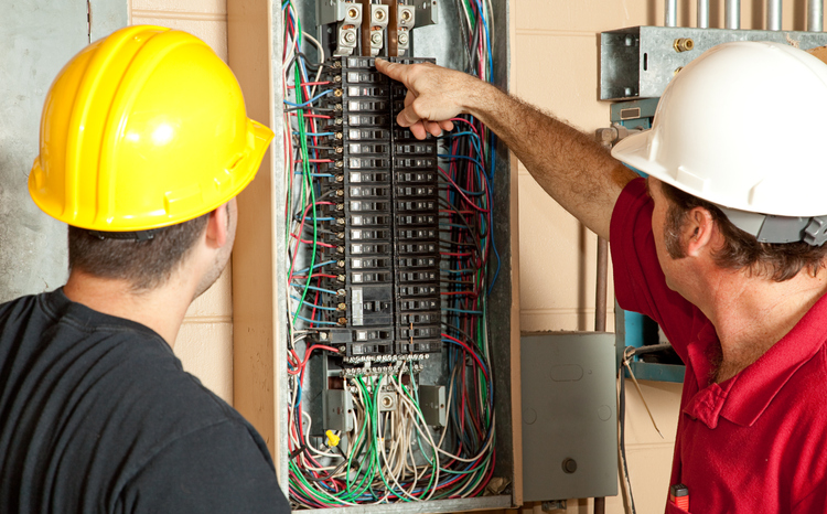 Two electricians performing electrical upgrades on a panel.