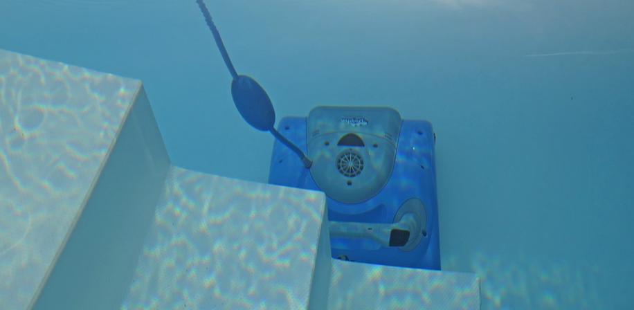 A blue pool noodle is floating in the water near an automatic pool cleaner.
