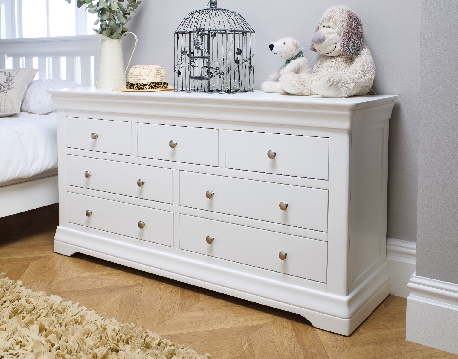 A white chest of drawers in a bedroom with a bird cage.