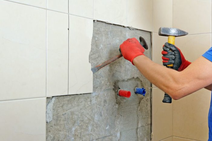 A man is hammering a kitchen tile into a wall for the backsplash.