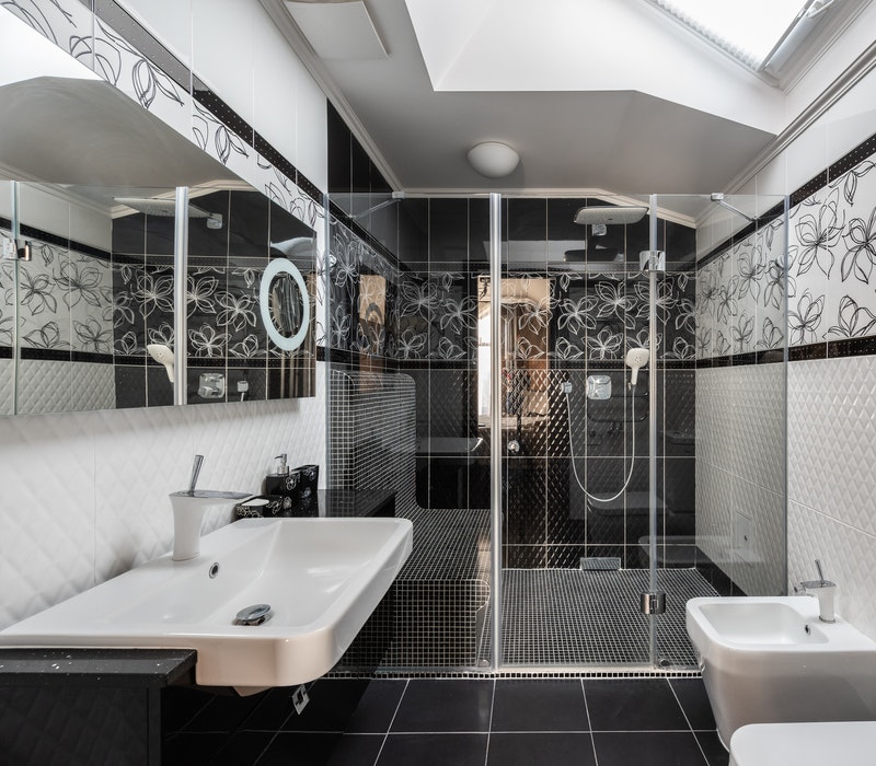 A black and white bathroom with a skylight and glass shower doors.