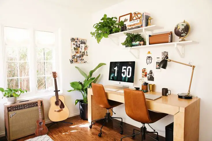 A home office with an acoustic guitar and a desk.