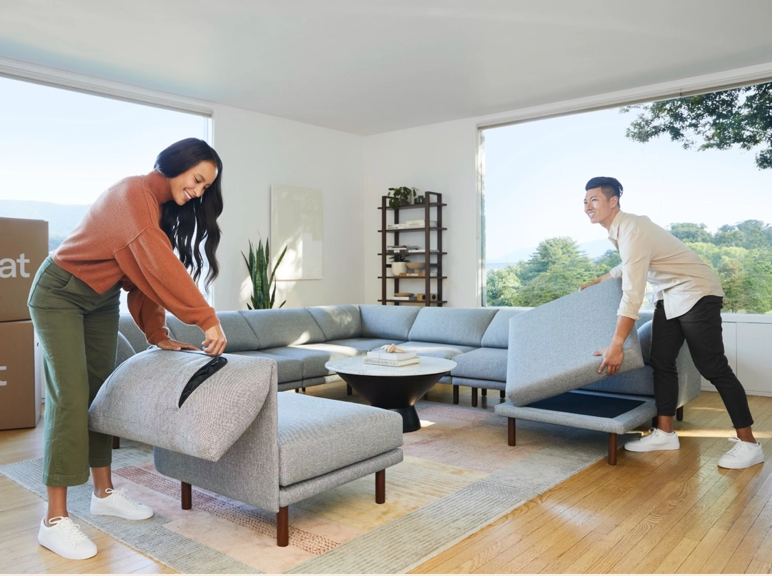 Two people rearranging new furniture in a living room.