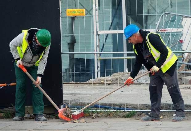 Two construction workers performing job site clean-up on a sidewalk.