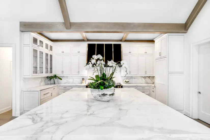 A white kitchen with marble counter tops and wooden beams.