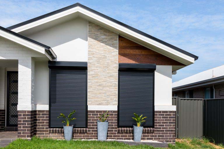 A house with black roller shutters and a potted plant.