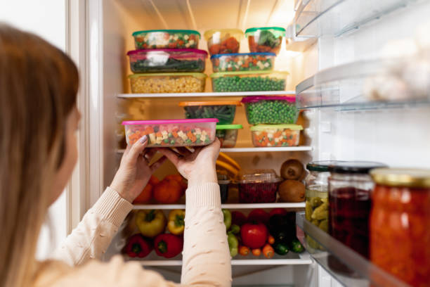 A woman is saving money by putting food into a refrigerator.