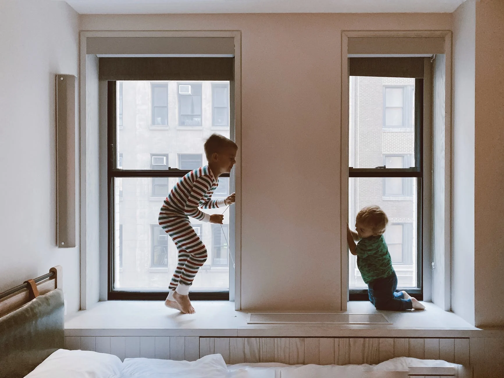 Two children playing on a bed in a hotel room.