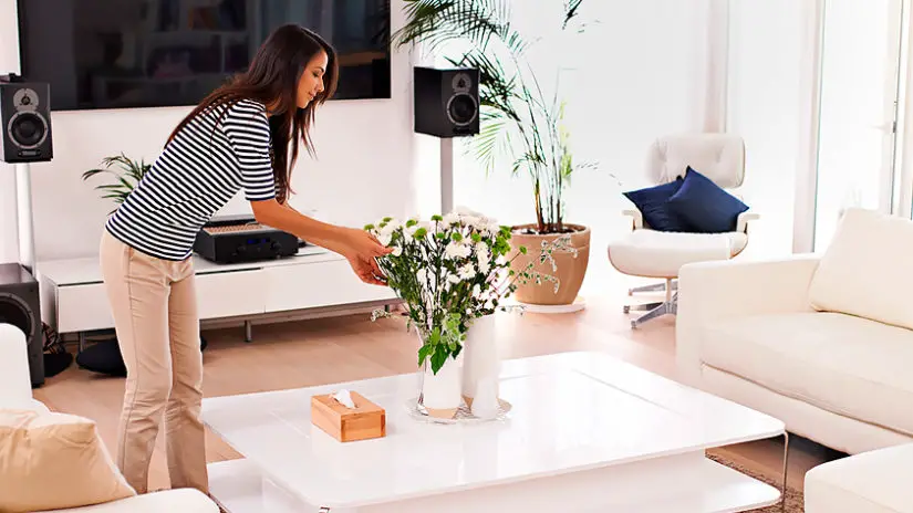 A woman putting flowers in a vase in a living room.