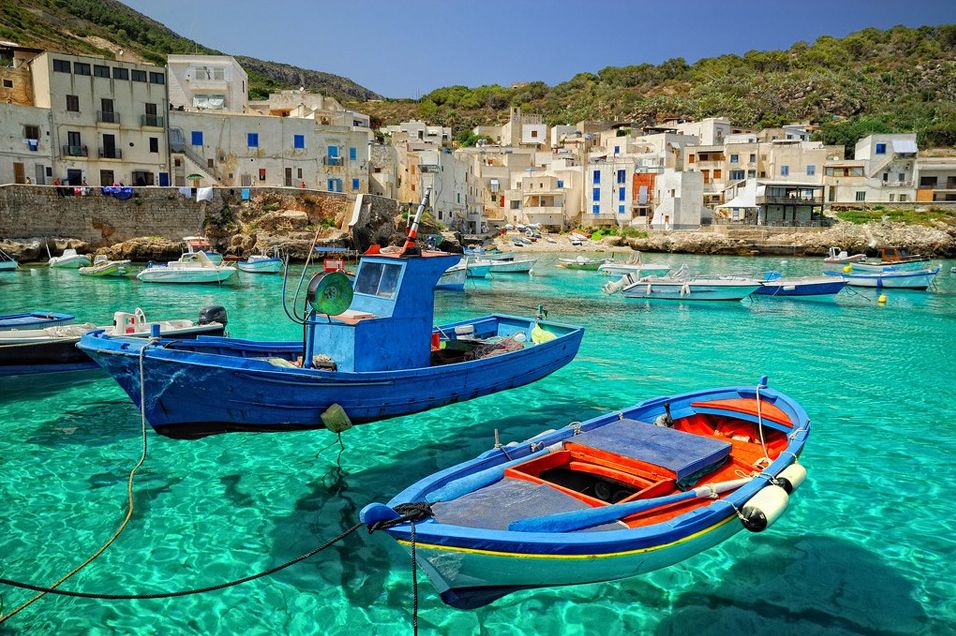 A blue boat docked in clear Sicilian waters.
