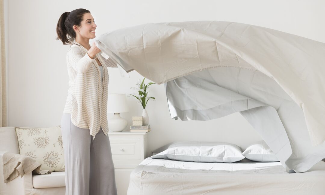 A woman is placing bed sheets on her bed.