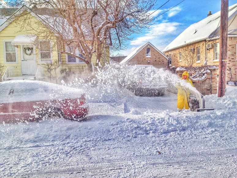 A man in a yellow jacket is using snowblowers to remove snow from a street.