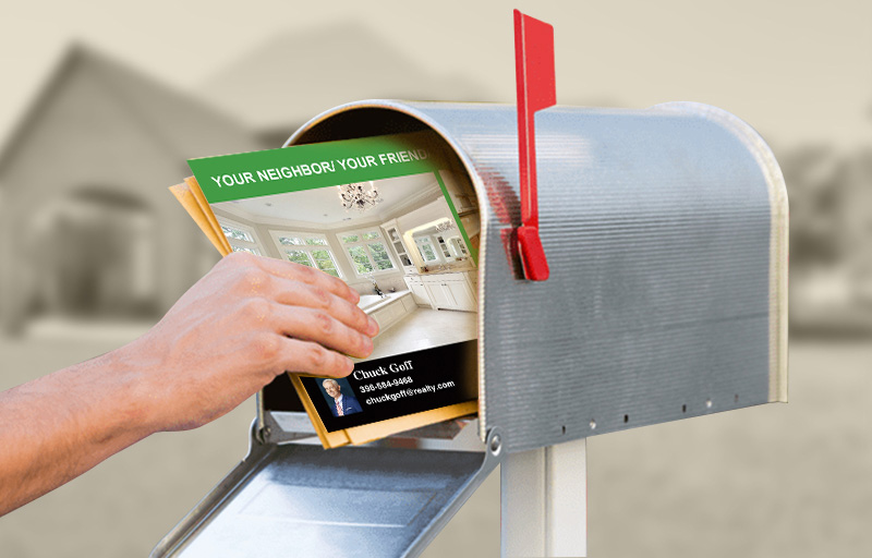 A hand is holding a real estate magazine out of a mailbox.