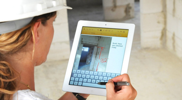 A woman wearing a hard hat is holding an iPad with an app designed for local contractors.