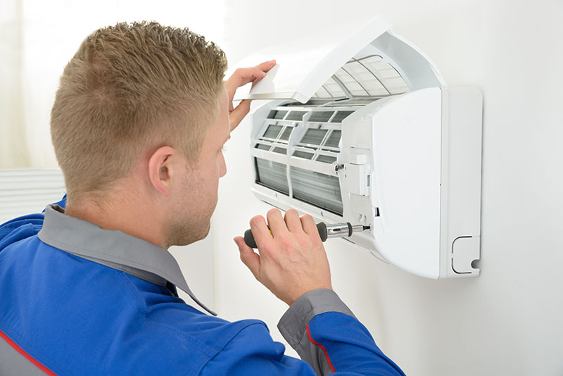 A man performing specialized AC repairs on a wall-mounted air conditioner.