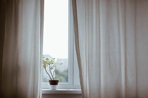 A window with curtains and a plant in a pot helps reduce cooling costs.