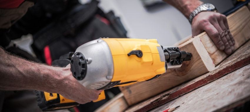 A man is using a nail gun on a piece of wood.