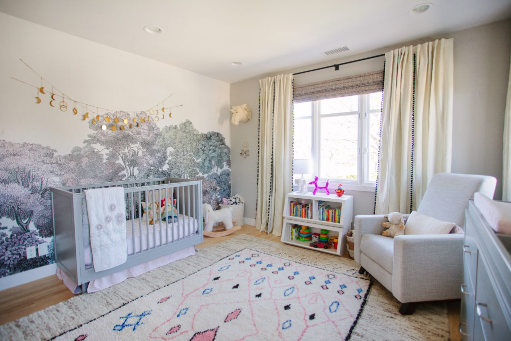 A nursery with a large mural on the wall and nursery rugs.