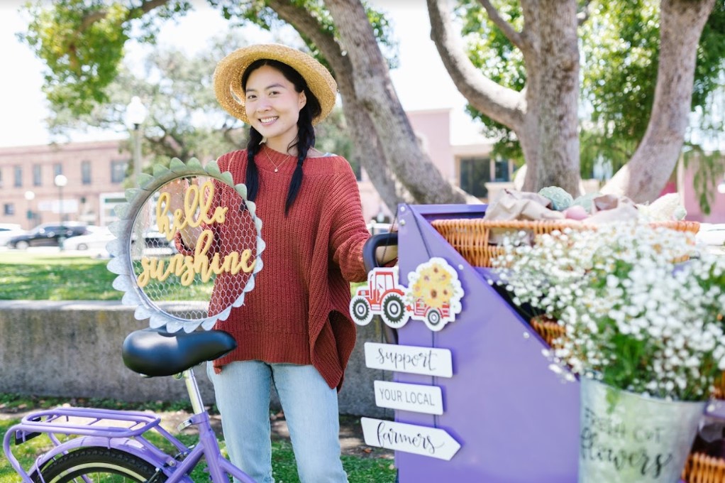 A woman is standing next to a purple bicycle with a pop-up reklamu sign on it.