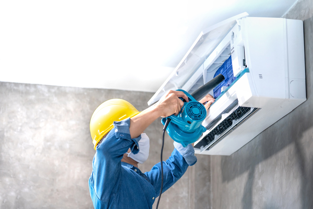 Keywords: AC Repair, air conditioner. 

Modified description: A man in a hard hat is repairing an air conditioner.