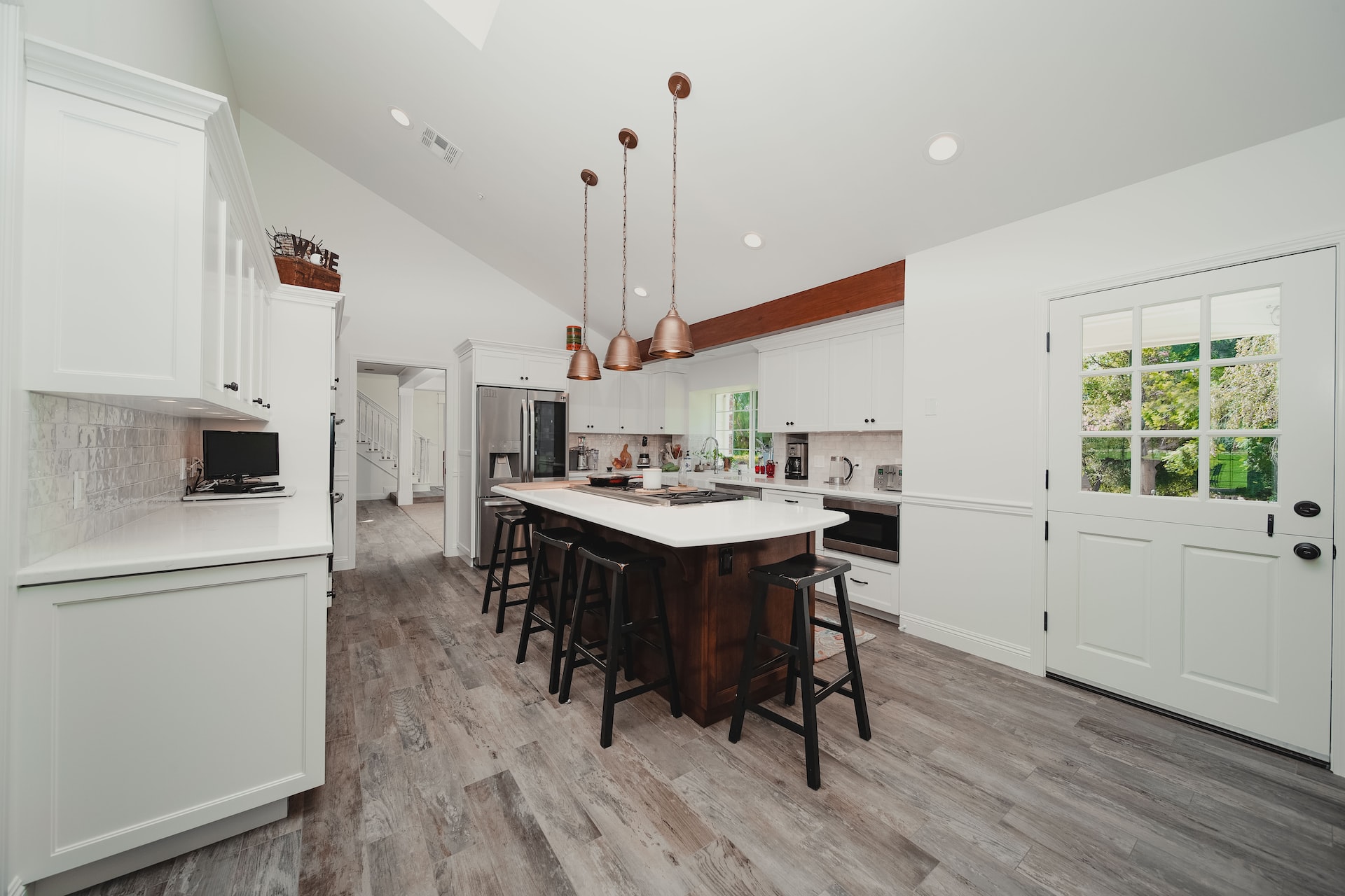 A white kitchen with wood floors and a center island incorporating copper accents.