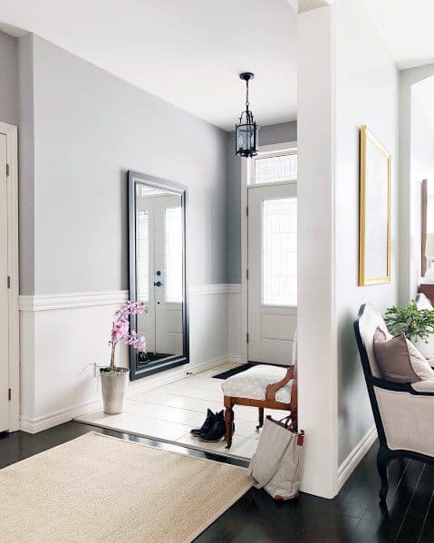A white and gray entryway with a bench and a mirror featuring dado rails.