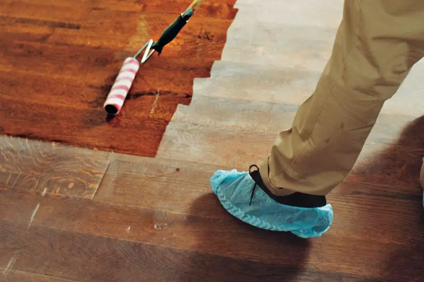 A person wearing blue gloves is painting a wooden floor.