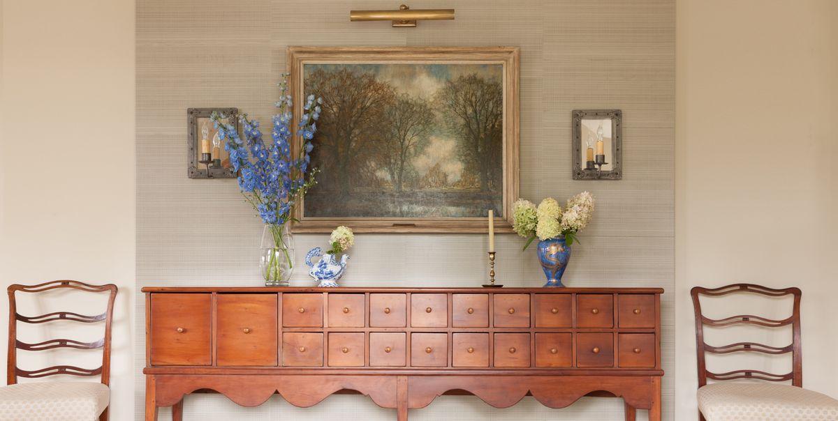 A vintage sideboard with two chairs and a painting.