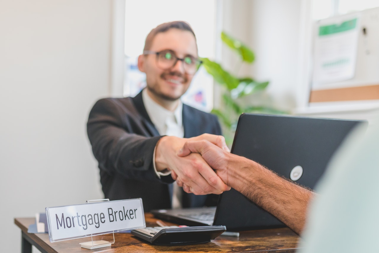 A man shakes hands with a sustainable mortgage broker in front of a laptop.
