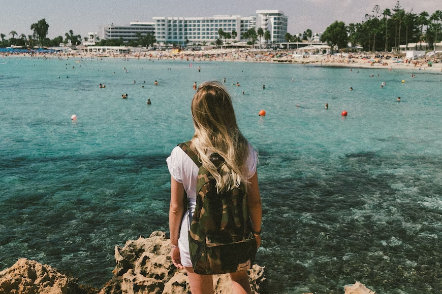 A woman with a backpack standing on a rock overlooking a beach showcasing hunting bag essentials.