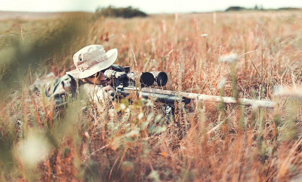 A man with a rifle in a field hunting.