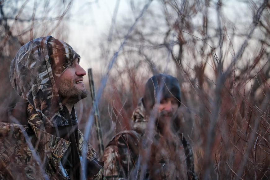 Two hunters in camouflage in the woods showcasing essential hunting bag items.