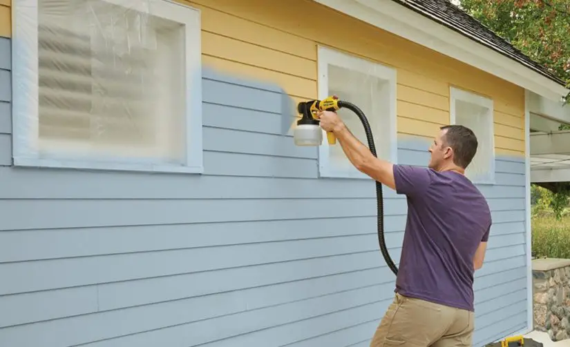 A man painting a house with a paint sprayer.
