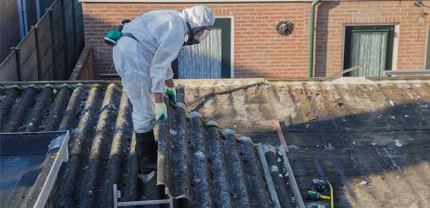 A man in a protective suit removing asbestos from a roof.